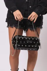 Cartera tipo baguette color negro, de cuero sintético con tachas plateadas y correa de cadena metálica.