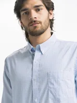 Camisa celeste y blanca a rayas verticales, de manga larga y corte clásico. Tiene cuello abotonado y bolsillo en el pecho.