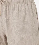 Bermuda de microfibra color beige, con cintura elástica y cordón ajustable. Presenta textura en el tejido y un bolsillo lateral.
