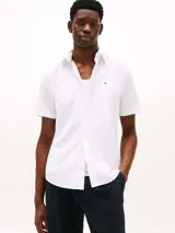 Camisa de manga corta blanca de Tommy Hilfiger confeccionada con popelín elástico de algodón BCI, con cuello abotonado, cierre con botones, detalles distintivos de Tommy Hilfiger y logo de Tommy Hilfiger bordado en el pecho.