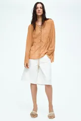 Blusa de gasa color ocre con estampado de piel de serpiente, escote en V pronunciado con tiras diagonales y mangas extralargas acampanadas.