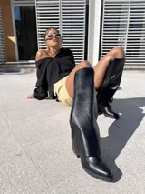 Botas negras de ecocuero, estilo texanas, de caña alta y taco cuadrado.