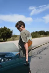 Remera color verde militar de manga corta con estampado en la espalda de un paisaje con montañas y sol. Corte clásico.