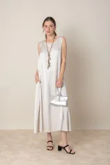 Vestido italiano color blanco hueso, modelo sin mangas con bolsillos laterales y corte suelto. Incluye un collar largo con dijes de piedras de colores y una cartera plateada con asa rígida.