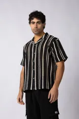 Camisa de hombre tejida al crochet con rayas verticales negras sobre base cruda, de manga corta y cuello camisero. Cierre frontal con botones.