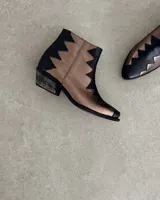Botín de cuero vacuno color bronce con puntera y caña en cuero negro. Diseño con borde superior en zigzag y taco de madera.