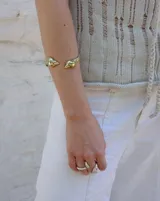 Brazalete rígido dorado con forma de caracola en los extremos.