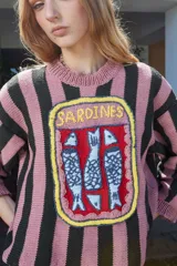 Sweater tejido a rayas horizontales rosas y negras, con cuello redondo y bordado frontal de una lata de sardinas con tres pescados.