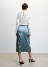 Falda midi cruzada color celeste, de tejido satinado y fluido, con abertura lateral, cierre lateral de cremallera, tiro medio, detalle fruncido y cierre de lazo lateral.