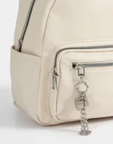Mochila urbana negra de cuerina con bolsillo frontal con cierre y charm colgante de cadena con dije de corazón y candado. Tiene correas regulables, manija superior, cierre superior, doble bolsillo frontal (uno con charm metálico) y bolsillos laterales.