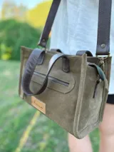 Cartera bandolera de cuero color verde oliva, con forro de tela, bolsillo delantero con cierre y bolsillo interno. Tiene correa larga regulable y manijas cortas.