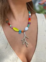 Collar corto con cuentas de cristal checo, cerámica y piedras reconstituidas de colores. Incluye separadores de acero quirúrgico y un dije plateado en forma de coral. Se cierra con cadena de acero quirúrgico para regular el largo.
