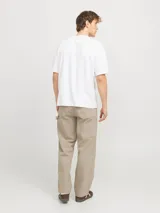 Pantalón jean color arena, de corte amplio, tiro alto y diseño de carpintero con múltiples bolsillos.