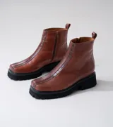 Botas cortas color marrón de cuero vacuno con suela track negra de goma. Presentan cierre lateral con cremallera YKK y puntera cuadrada.