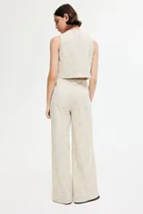 Pantalón de corte holgado color beige, en tejido texturizado con pliegues adelante y atrás. Modelo de tiro alto con elástico oculto en la cintura y piernas anchas. Bolsillos delanteros decorativos con botón de metal con diseño.