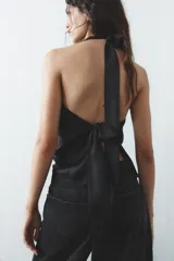 Top negro de satén con cuello halter drapeado ajustable con lazada en el cuello y espalda descubierta con lazada.