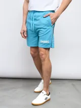 Bermuda deportiva celeste de piqué con cintura elástica ajustable con cordón, bolsillos laterales y logo Umbro estampado en blanco en la pierna izquierda.