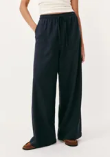 Pantalón de lino color crema, de corte recto y tiro alto, con cintura elástica ajustable con cordón y bolsillos laterales.