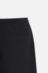 Pantalón negro de corte cropped, con cintura elástica ajustable con cordón, bolsillos laterales y traseros de vivo. El bajo tiene terminación con vuelta.