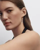 Aro individual dorado con dije colgante de cristal de roca transparente en forma cilíndrica.