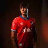 Camiseta de fútbol Umbro del Club Nacional de Football, modelo Away 1 2025. Diseño rojo con detalles en azul en cuello y mangas. Incluye logo de Umbro, escudo del club y sponsors en el frente.
