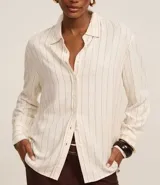 Camisa de viscosa y lino color crudo con finas rayas verticales azules, cuello clásico, mangas largas con puños abotonados y cierre frontal con botones.