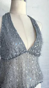 Top halter gris claro, ajustado al cuerpo, con escote pronunciado en V y cubierto de lentejuelas plateadas. El tejido es semitransparente.