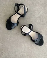 Sandalias bajas negras con tiras finas cruzadas y tobillera con hebilla.