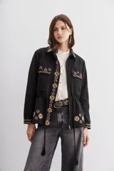 Campera negra de algodón con bordados de flores y lentejuelas. Tiene corte recto, ajuste interno en la cintura, bolsillos con solapa y cierre frontal.