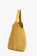 Bolso de hombro amarillo con cuerpo en relieve efecto trenzado, asa de hombro, cartera interior con cierre mediante cremallera metálica, base rígida con tachas y cierre mediante botón imantado.