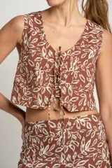Chaleco marrón con estampado de hojas blancas, escote en V y lazo ajustable en el centro.