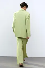 Pantalón verde claro de tiro alto con trabillas y botón en la cintura. Tiene pliegues, bolsillos laterales y falsos bolsillos de vivo en la espalda. El cierre frontal es con cremallera, botón interior y ganchos metálicos.