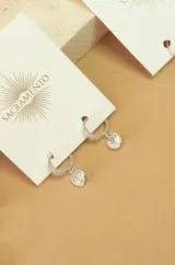 Aros tipo argolla plateados con pequeños strass y dije colgante de cristal transparente en forma de corazón.