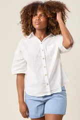 Camisa color beige claro, de corte clásico, con cuello, botones frontales, bolsillo en el pecho y mangas tres cuartos con presilla para sujetar.