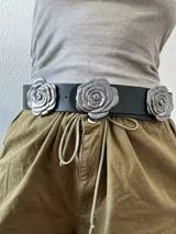 Cinturón negro de cuero sintético con tres hebillas plateadas en forma de rosa.