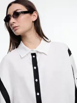 Camisa de lino color negro con silueta amplia y mangas 3/4. Diseño con tiras de color blanco en contraste en la cartera, mangas y cuerpo. Tiene tajos laterales y ruedo irregular en el frente.