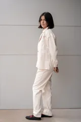 Chaqueta blanca de jean con cuello clásico, cierre frontal con botones metálicos y bolsillo de parche en el pecho. Presenta detalles de piedras de colores en el canesú.