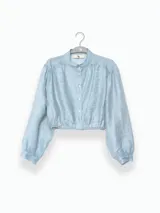 Blusa corta celeste de tejido arrugado liviano, con cuello mao, botones al frente, mangas abullonadas y ruedo elastizado.