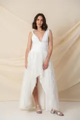 Vestido blanco de crepe con escote profundo y falda irregular con flecos brillantes. Se puede usar con pantalones por debajo.