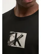 Remera negra de algodón con cuello redondo y mangas cortas. Presenta el logo de Calvin Klein estampado en el pecho dentro de un recuadro blanco con efecto desgastado.