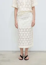 Falda midi color crudo con diseño calado de flores en relieve, tiro medio, corte recto, abertura lateral y cierre de cremallera lateral. Incluye forro interior.