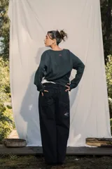 Crewneck (jersey de cuello redondo) unisex color gris oscuro, con estampado frontal que dice "RE:SKIN" y texto pequeño debajo. Presenta mangas largas y corte holgado.