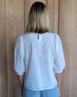 Remera blanca de algodón con mangas 3/4 abullonadas y cuello redondo. Presenta costuras a contratono en ruedo y cuello.