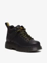 Botín de cuero negro Dr. Martens modelo Woodard, con cuello acolchado, cordones de tipo excursionista en amarillo y negro, suela acanalada Club Wedge con pespunte negro y tirador trasero con logo.