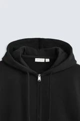 Sudadera negra relaxed fit confeccionada en tejido de algodón compacto con interior en rizo. Cuello con capucha ajustable y manga larga. Bolsillos frontales tipo canguro. Acabados en rib. Cierre frontal con cremallera.