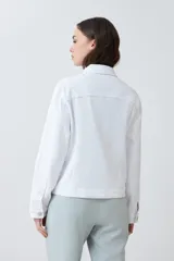 Campera de jean blanca con cuello clásico, bolsillos con solapa abotonados en el pecho y cierre frontal con botones metálicos. Corte recto.