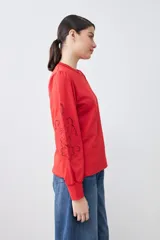 Sweatshirt rojo de manga larga con cuello redondo y calados bordados en los hombros y mangas.
