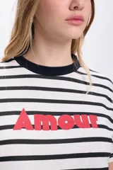 Remera de manga corta con cuello redondo y estampado a rayas horizontales en blanco y negro. Tiene la palabra 'Amour' estampada en rojo.