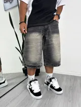 Bermuda de jean color negro gastado, tiro bajo y corte ancho (baggy), con bordado blanco en la parte trasera del bolsillo.