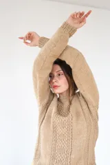 Suéter tejido a mano color arena, con manga raglán y cuello semi alto. El diseño incluye un delicado juego de puntos que dibujan textura y un ruedo con forma ondulante.